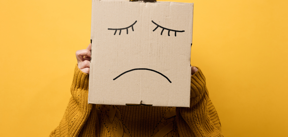 Person holding a sad face sign to represent depression symptoms and the need for psychological evaluation support.